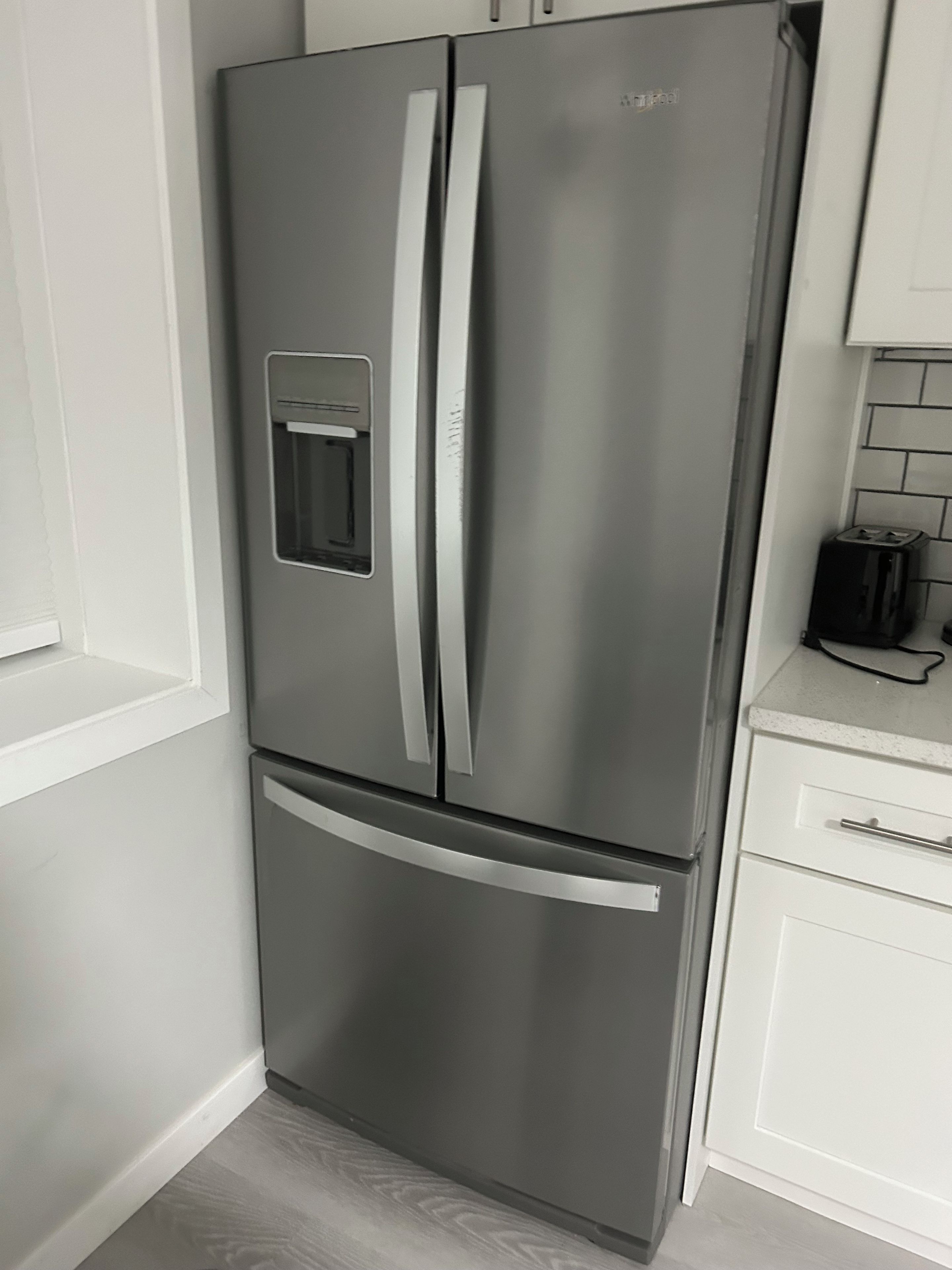 A stainless steel double-door refrigerator with a freezer compartment below, situated in a kitchen with white cabinetry and a tiled backsplash.