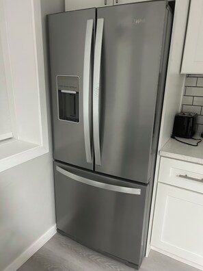 A stainless steel double-door refrigerator with a freezer compartment below, situated in a kitchen with white cabinetry and a tiled backsplash. - Charming & Peaceful Home Away From Home (Calgary)
