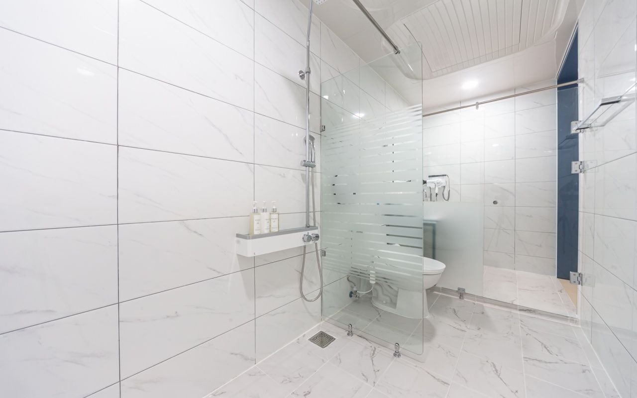 A modern bathroom with a glass-enclosed shower, a glass partition, and a white marble floor.