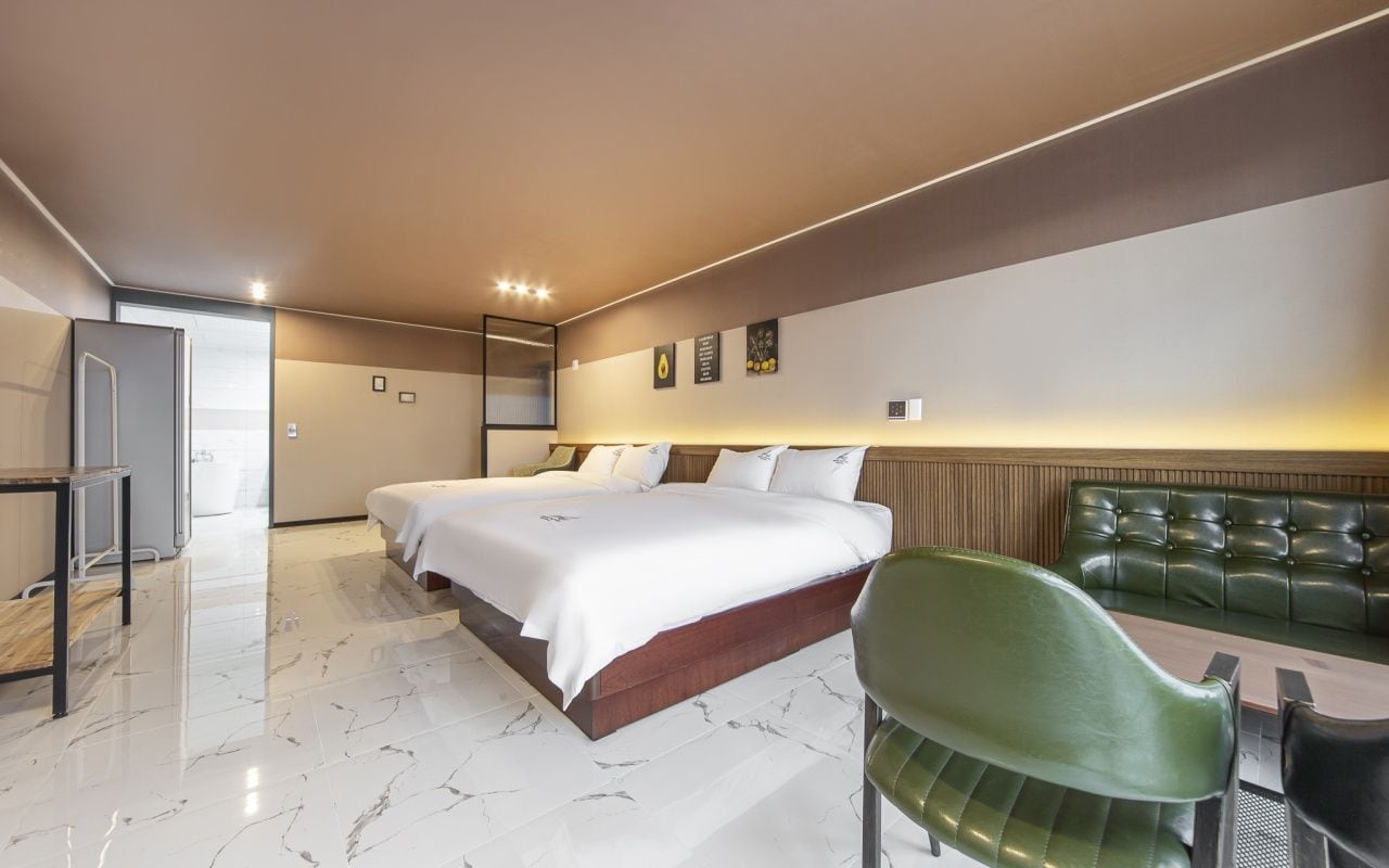 A hotel room with a large bed, a green chair, a small table, and a view of the sea.