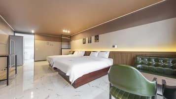 A hotel room with a large bed, a green chair, a small table, and a view of the sea.