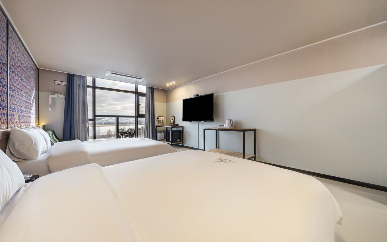 Quarto de hotel com uma cama grande, televisão, escrivaninha e vista da cidade.