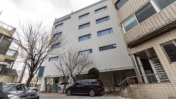Hotel de vários andares com fachada moderna, várias janelas e área de estacionamento com carros.