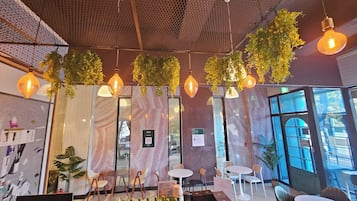A restaurant interior with hanging plants, pendant lights, and a bar area with bottles and glasses.