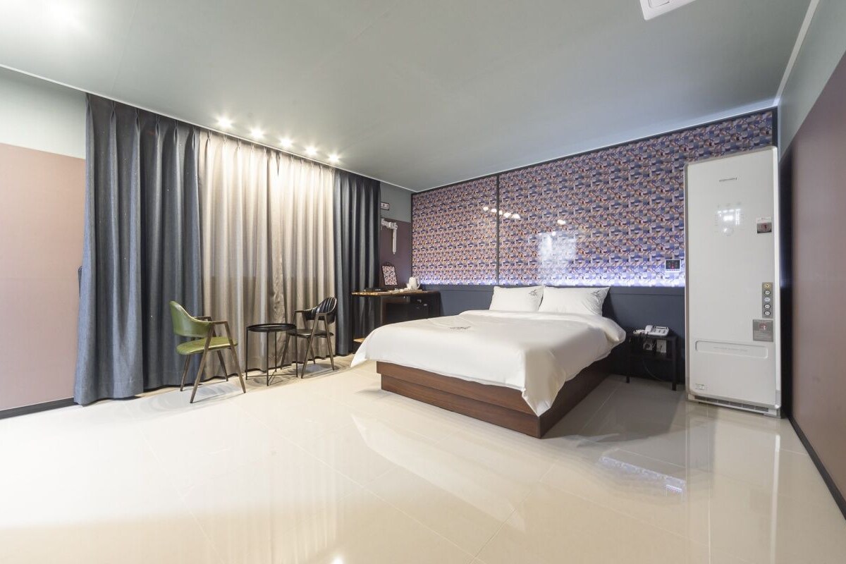 Een moderne hotelkamer met een groot bed, een bureau met stoel, een kledingkast en een behang met patroon.