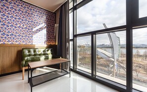 A modern room with a large window, a green leather sofa, a wooden table, and a patterned wall. - Aria Business Hotel (Pohang)