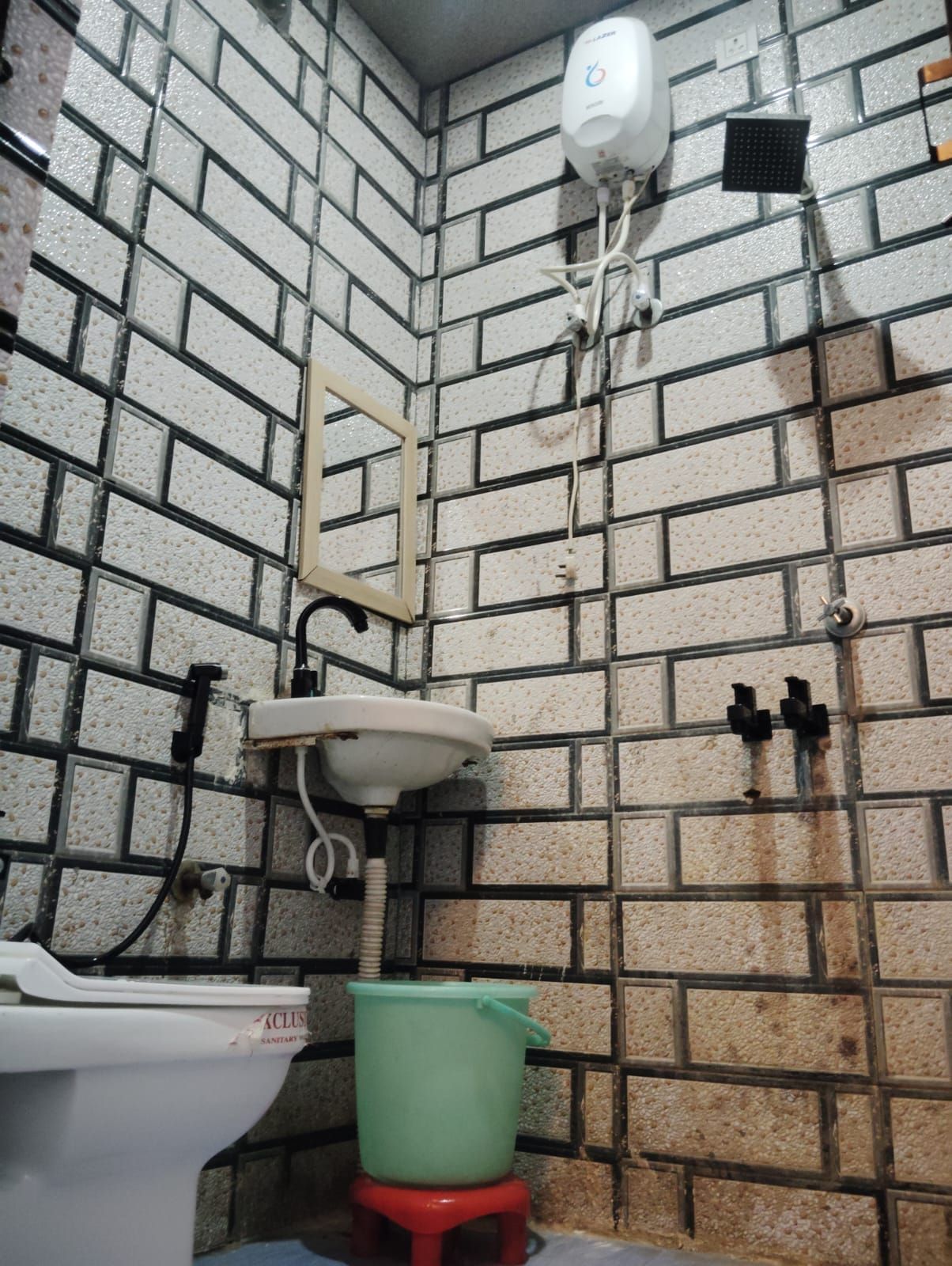 A bathroom with a white toilet, a green bucket, and a white sink.