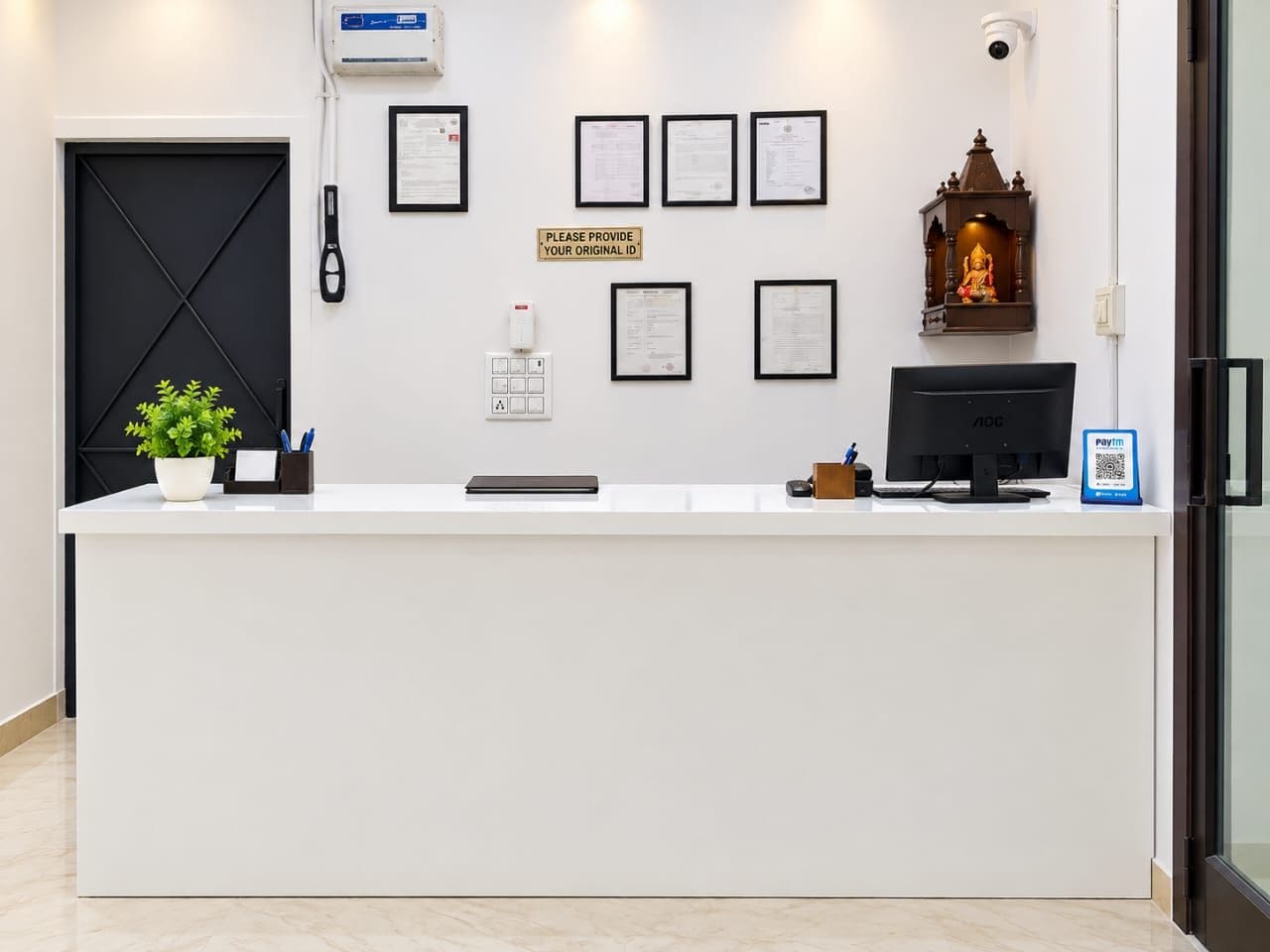 A reception desk with a computer, framed documents, a sign requesting ID, a plant, and a small statue.