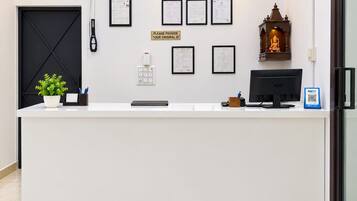 A reception desk with a computer, framed documents, a sign requesting ID, a plant, and a small statue.