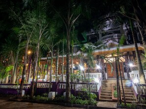 A building with a staircase leading to a balcony, surrounded by palm trees and illuminated by lights. - Palmera Gardens Hotel Murang'a (Murang'a)