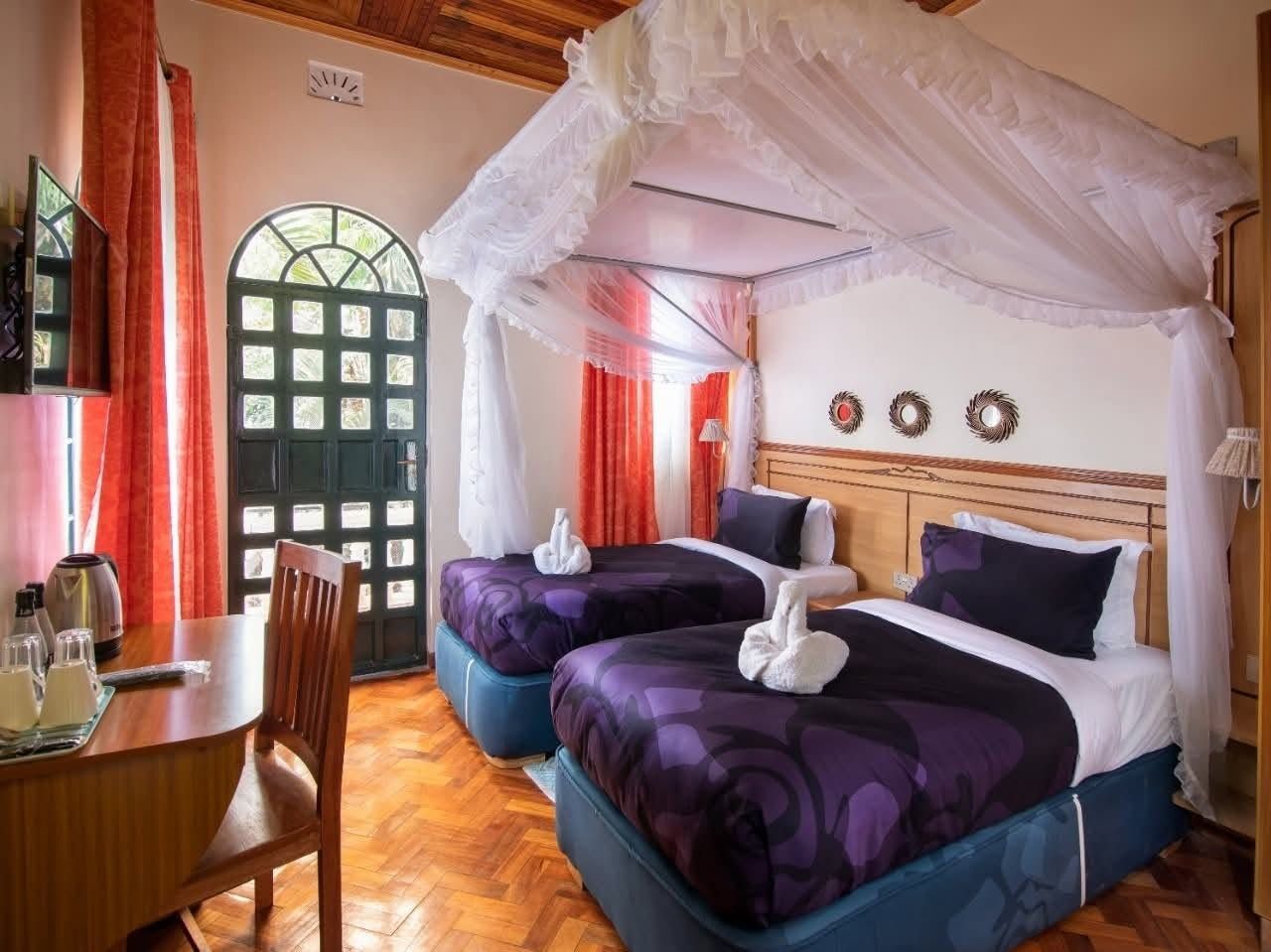 Una camera d'albergo con due letti, un tavolo da pranzo e una finestra con tende.