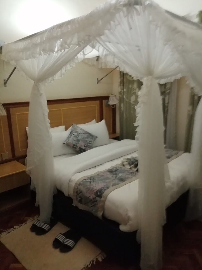 A bed with a canopy, a nightstand, and a pair of slippers.