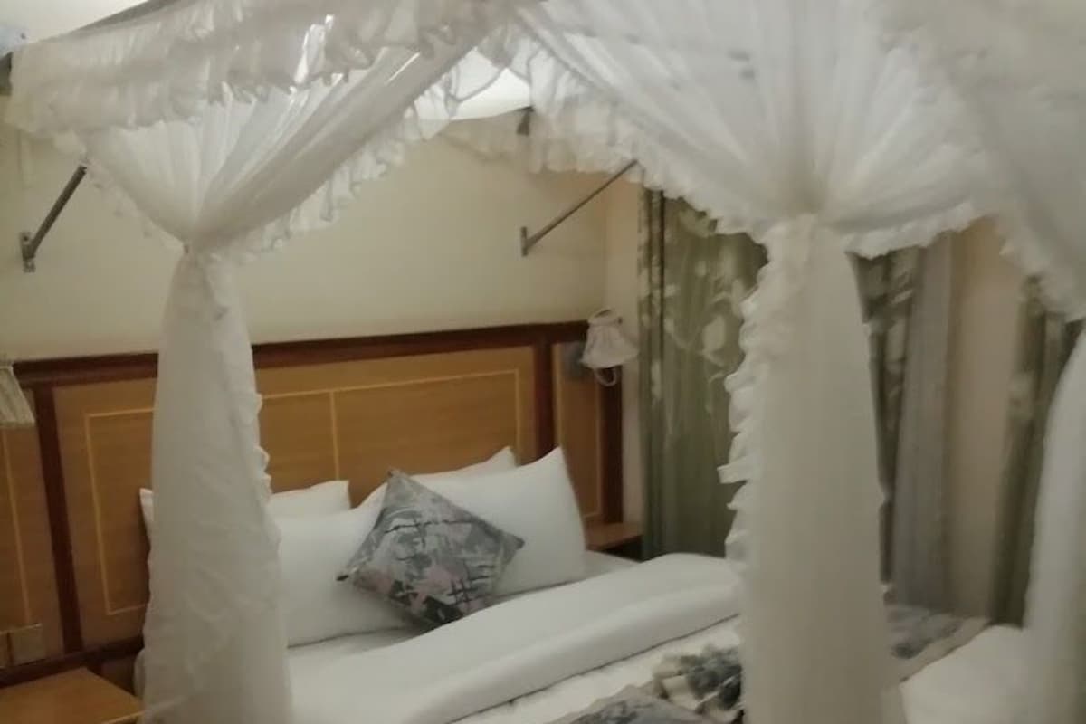 A bed with a canopy, a nightstand, and a pair of slippers.