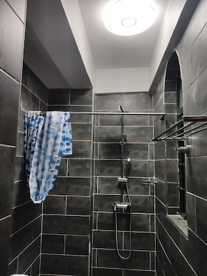 A modern shower with dark tiles, a visible shower head, and a towel rack. - Palmera Gardens Hotel Murang'a (Murang'a)