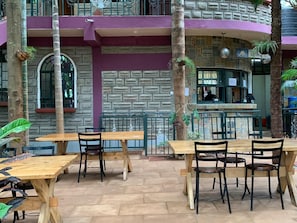 Un café en plein air avec des tables et des chaises en bois, des murs en pierre et un espace bar.