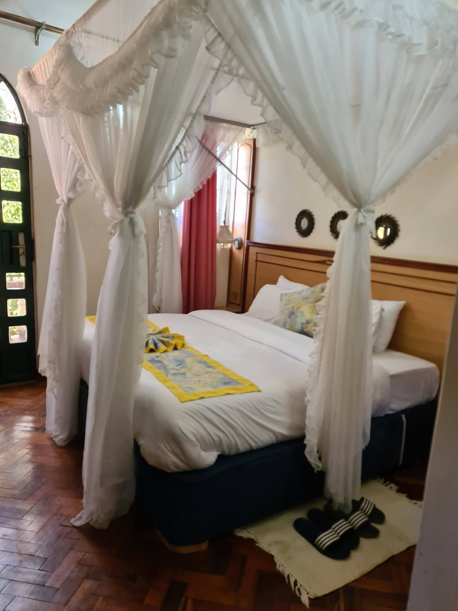 Una habitación con cama, mesita de noche, suelo de madera y ventana con cortinas.