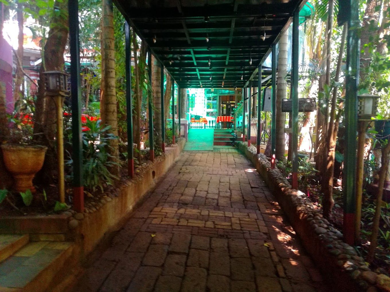 Un corridoio coperto con un percorso in mattoni, immerso nel verde e decorato con piante in vaso.