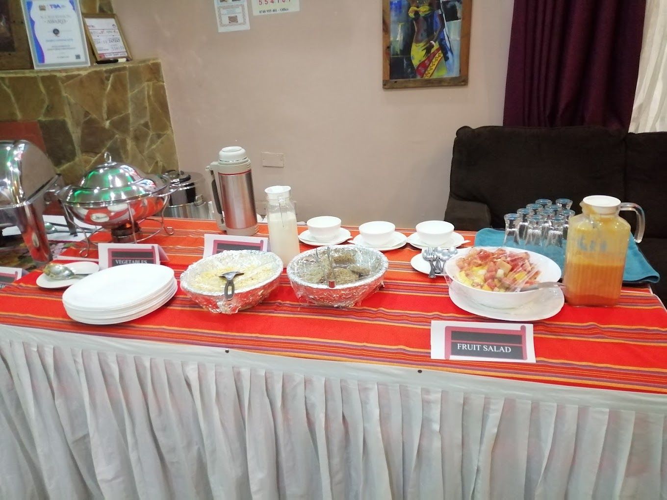 Un tavolo per buffet con aree dedicate a verdure, insalata di frutta e una caraffa per bevande.