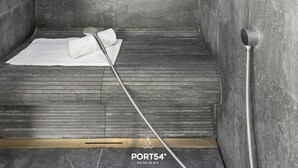 Moderni suihku, jossa on harmaat laatat, käsisuihkupää ja pyyhe lattialla.