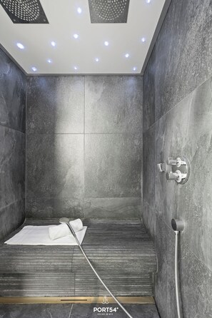 A modern shower with grey tiles, a handheld showerhead, and a towel on the floor. - Spacious holiday apartment with luxury features and covered terrace near the Bal (Lübeck)