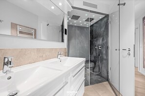 A modern bathroom with a large white sink, a glass shower enclosure, and a beige tiled floor. - Spacious holiday apartment with luxury features and covered terrace near the Bal (Lübeck)