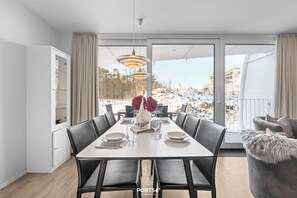 A modern dining room with a large table, black chairs, and a view of a snowy landscape through large windows. - Spacious holiday apartment with luxury features and covered terrace near the Bal (Lübeck)