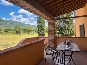 A covered outdoor dining area with a table set for two, overlooking a scenic landscape. - Casale Paradisino - Appartamento Il Sole (Castiglion Fiorentino)