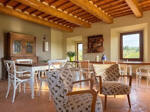 A spacious dining area with a high wooden ceiling, white chairs, and a table set for dining. - Casale Paradisino - Appartamento Il Sole (Castiglion Fiorentino)