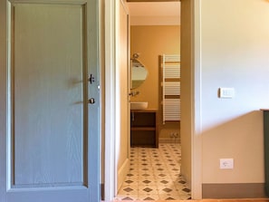 A hallway leading to a bathroom with a tiled floor, a sink, and a mirror. - Casale Paradisino - Appartamento Il Sole (Castiglion Fiorentino)