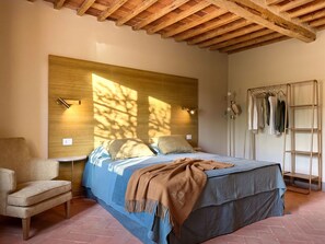 A bedroom with a bed, a chair, a wardrobe, and a wooden ceiling. - Casale Paradisino - Appartamento Il Sole (Castiglion Fiorentino)