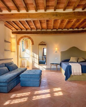 A room with a bed, a sofa, a bench, and a mirror. - Casale Paradisino - Appartamento Il Sole (Castiglion Fiorentino)