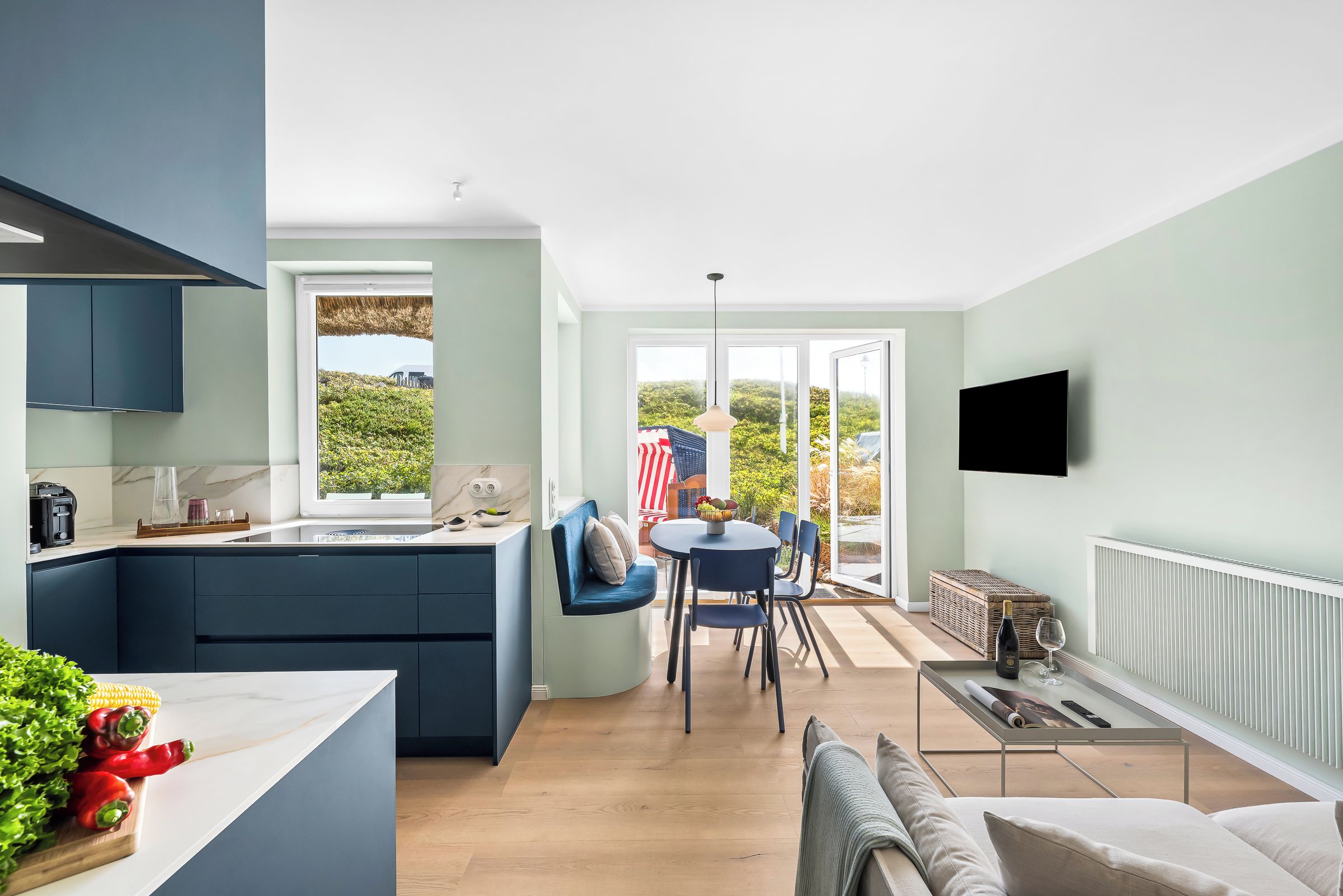 Eine moderne Küche mit Backofen, ein Essbereich mit Tisch und Stühlen sowie ein Wohnbereich mit Sofa und Wandfernseher.