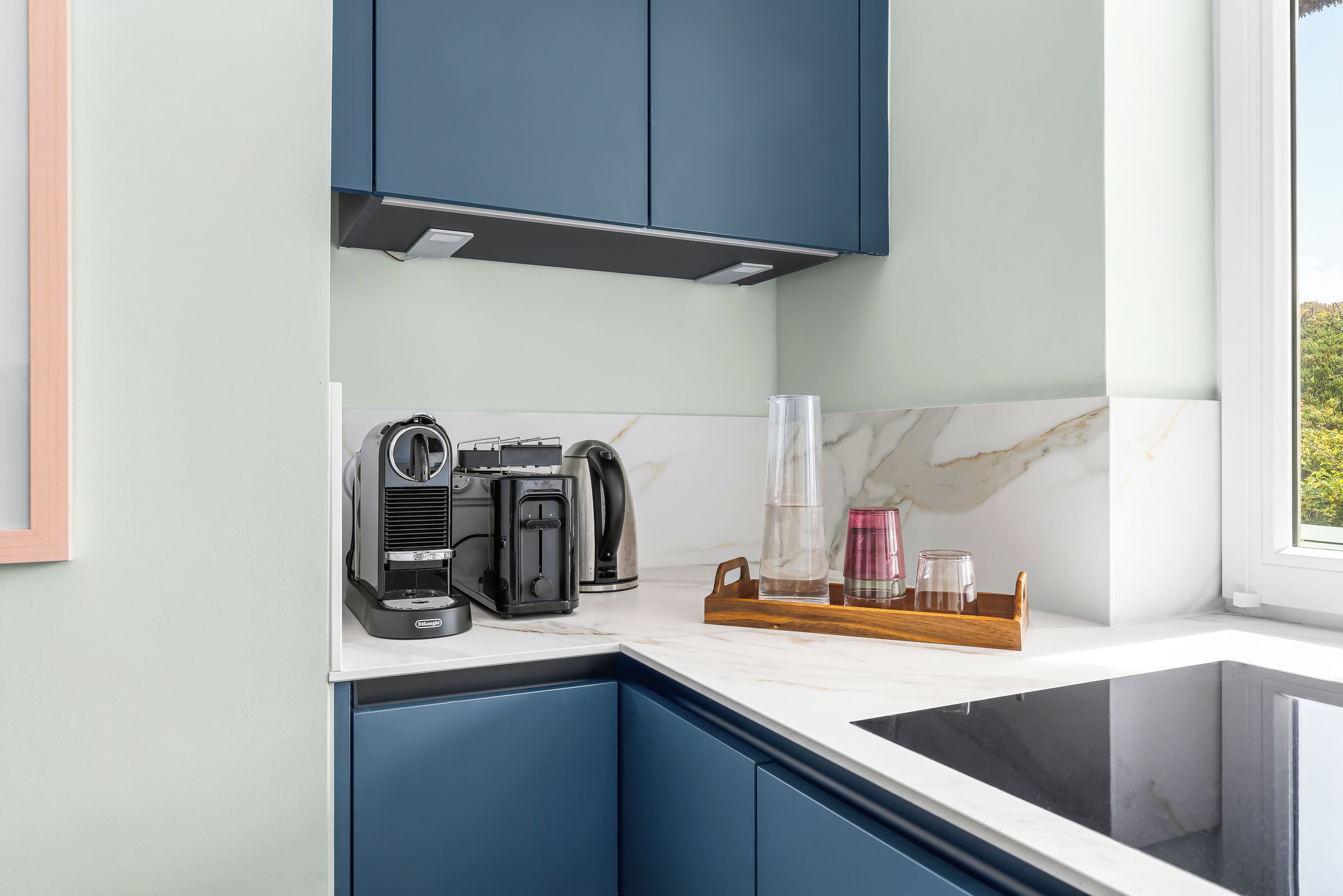 Eine Küche mit dunkelblauen Schränken, einer Kaffeemaschine, einem Toaster und einem Holftablett mit Gläsern.