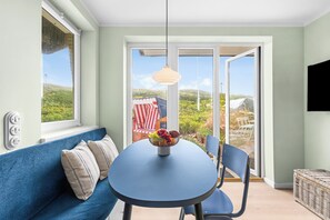 Une pièce avec un canapé bleu, une table ronde sur laquelle se trouve un panier de fruits, et une vue à travers une porte vitrée.