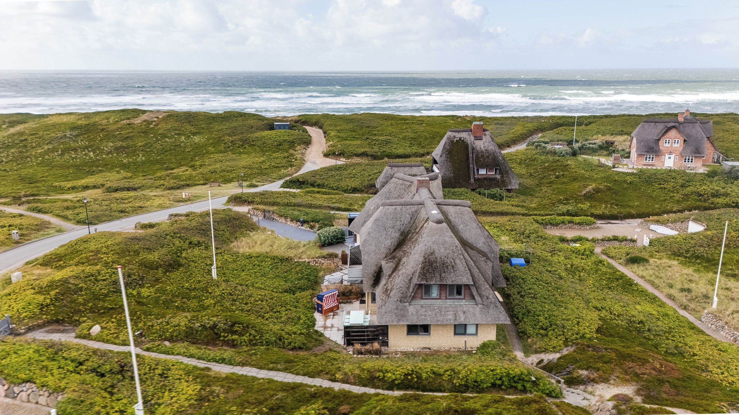 A coastal property with thatched-roof cottages, a paved pathway, and a view of the sea.