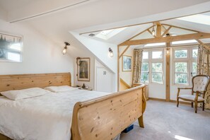 A bedroom with a wooden bed, a chair, and a window with curtains. - Holly Cottage - Beautiful 3 Bedroom Cottage near Bristol (Backwell)