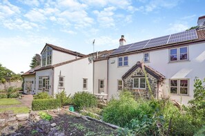 Ein zweistöckiges Haus mit Garten, Solaranlage und einem Anbau aus Stein.