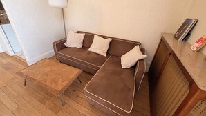 Un sofá marrón con cojines estampados, una mesa de centro de madera y una lámpara fijada a la pared.