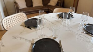 Una mesa de comedor preparada con platos, cubiertos y copas de vino, con un sofá y un aparador al fondo.