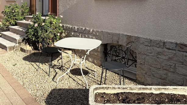 Un edificio con fachada blanca, una ventana, una puerta y un pequeño espacio al aire libre con una mesa y sillas.