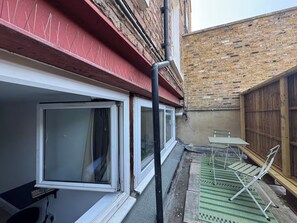 Una propiedad residencial con fachada roja, pared de ladrillo y un pequeño espacio al aire libre con un tapete verde y sillas metálicas.