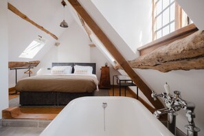 Une chambre avec une grande baignoire, des poutres en bois et un lit doté d’une tête de lit.