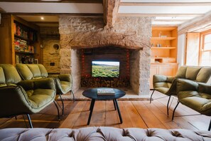 A cozy living room with a stone fireplace, leather armchairs, a round coffee table, and a bookshelf.