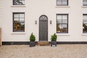 A building with a symmetrical facade, a central dark-colored door, and two potted plants on either side. - Elegant Escape at Dineter Wood House (Ewyas Harold)