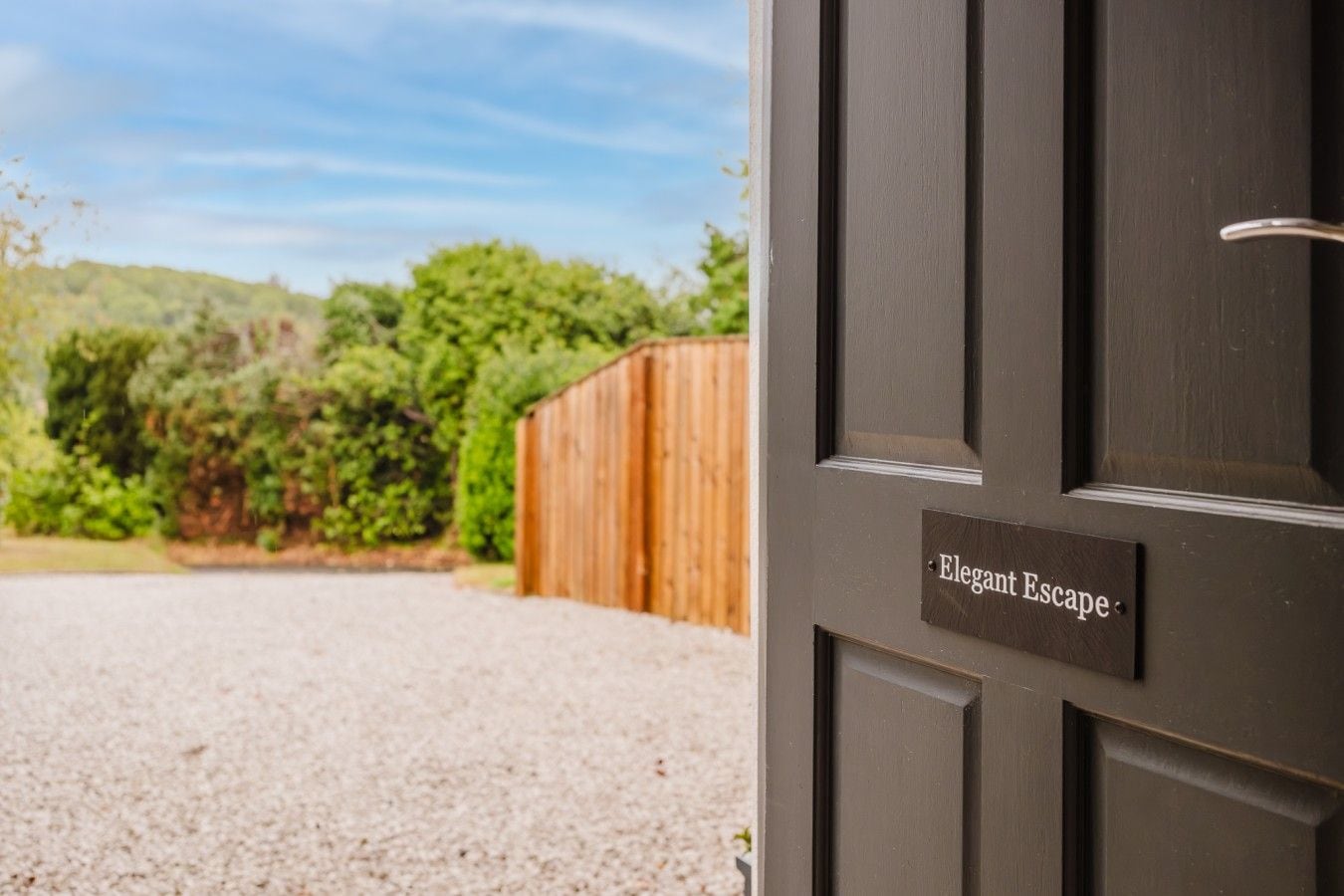 Eine Tür mit einem Schild mit der Aufschrift 'Elegant Escape' und einer Schotterauffahrt, die zu einem Holzzaun führt.