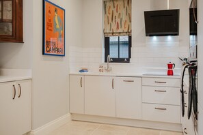 A kitchen with white cabinets, a window with patterned curtains, a black microwave, and a red coffee maker. - Elegant Escape at Dineter Wood House (Ewyas Harold)