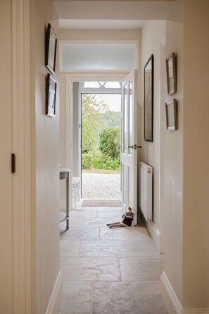 A hallway with a view to a garden, a radiator, and framed pictures on the walls. - Elegant Escape at Dineter Wood House (Ewyas Harold)