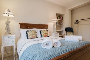 A neatly made bed with a blue knitted blanket, two bedside lamps, a wooden headboard, and a bookshelf with books. - Elegant Escape at Dineter Wood House (Ewyas Harold)