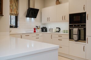A modern kitchen with white cabinetry, a black range hood, a coffee maker, and a kettle on the countertop. - Elegant Escape at Dineter Wood House (Ewyas Harold)
