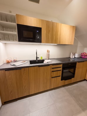 A modern kitchen with wooden cabinets, a black microwave, a sink with a faucet, and a dishwasher.